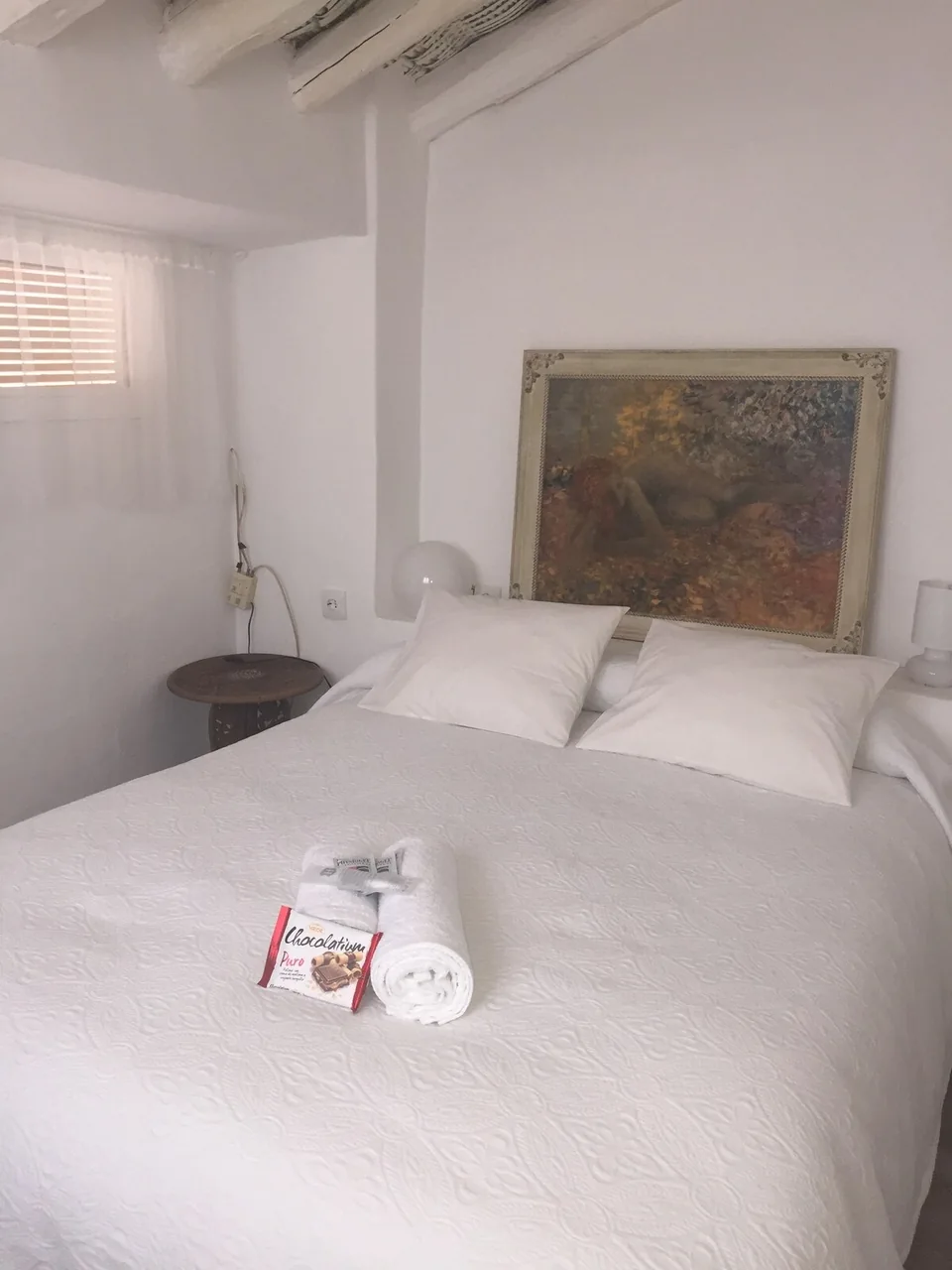 Habitación con cama doble, ropa blanca y cuadro sobre el cabecero